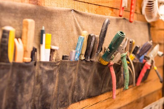 Old different tools in hanging canvas organizational wall mounted hardware storage with pockets in garage, selective focus