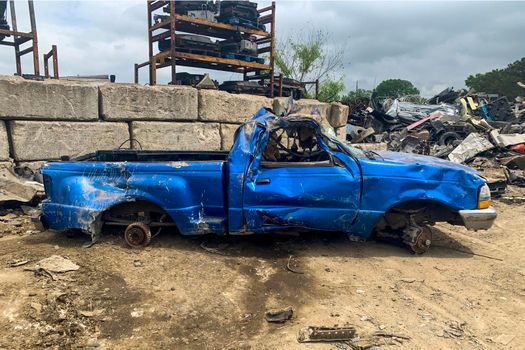 Side view of damaged blue pickup without wheels on the junkyard after car accident on a road, cemetery of cars, recycling broken automobiles