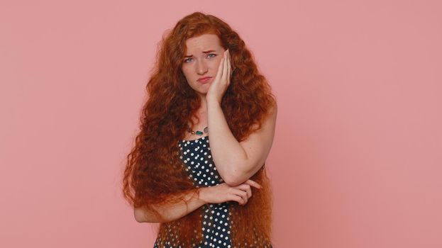 Dental problems. Young redhead woman touching cheek, closing eyes with expression of terrible suffer from painful toothache, sensitive teeth, cavities. Ginger girl with freckles on pink background