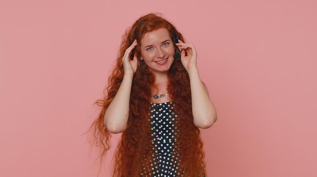 Smiling red hair girl wearing headset, freelance worker, call center or support service operator helpline, having talk with client or colleague, communication support. Young woman on pink background