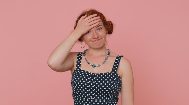 Face palm. Shame on you. Upset young redhead woman in dress making unhappy gesture, feeling bored, disappointed in result, bad news. Ginger girl with freckles isolated alone on pink studio background