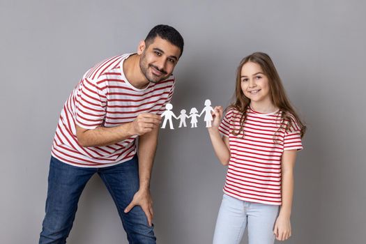 Portrait of father and daughter holding paper chain people together, happy family, relationships, childhood, parenthood, looking at camera with smile. Indoor studio shot isolated on gray background.