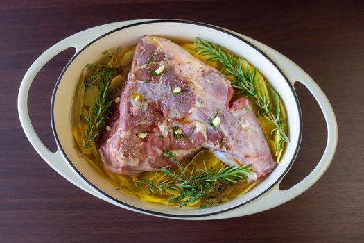 raw leg of lamb prepared to cook with sliced potatoes and provencal herbs, top view