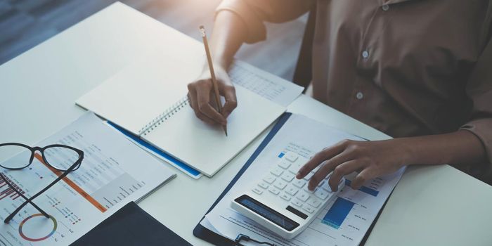 Business woman using calculator and writing make note with calculate. Woman working at office with laptop and documents on his desk.