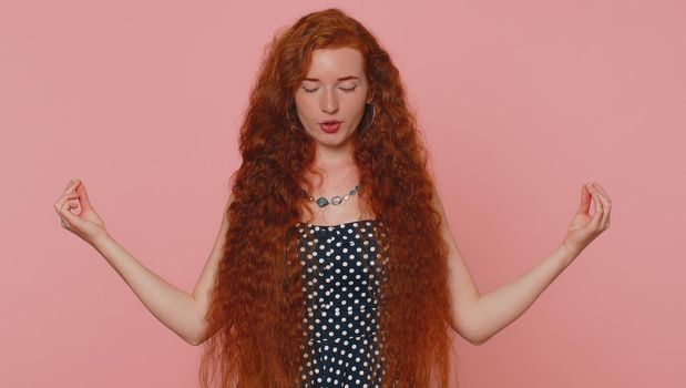 Keep calm down, relax, inner balance. Woman breathes deeply with mudra gesture eyes closed meditating with concentrated thoughts peaceful mind. Redhead freckles girl isolated on pink studio background