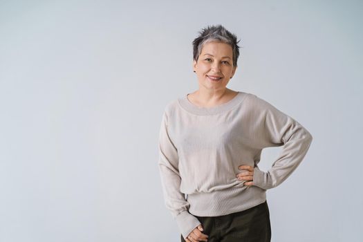 Happy smiling grey hair mature woman 50s posing shoulders slightly up and copy space on right isolated on white background. Copy space and place for product placement. Life care concept. Toned image.