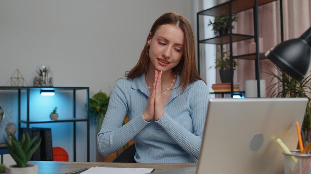 Young woman freelancer sitting at desk at home office pray to God ask for good luck in business, startup, upcoming negotiations. Faith, religion. Girl student study working online remote distance job