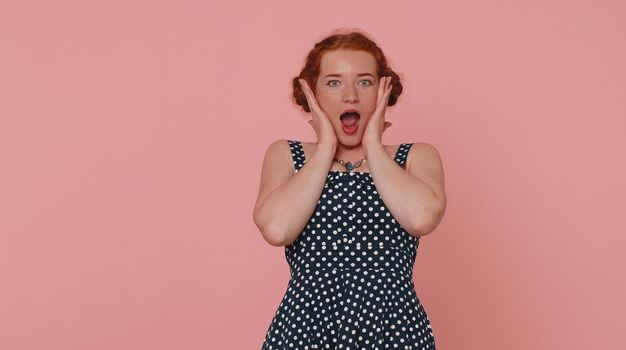 Oh my God, Wow. Excited amazed winner ginger woman raising hands in surprise looking at camera with big eyes, shocked by sudden victory. Sincere young girl isolated alone on pink studio background