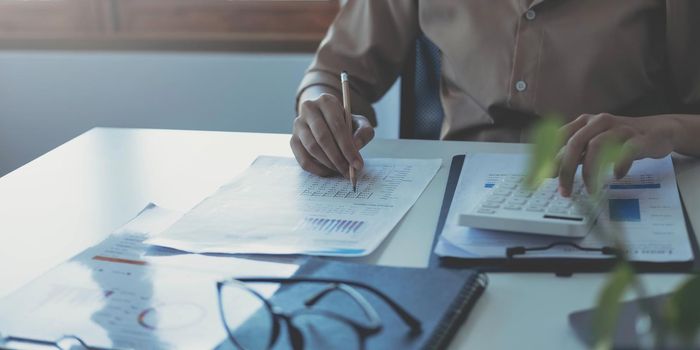 Business woman using calculator and writing make note with calculate. Woman working at office with laptop and documents on his desk.