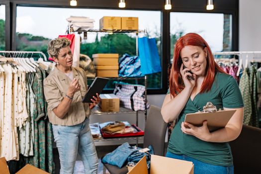 coworkers, working in the warehouse of the clothing shop, receiving calls from their customers and suppliers. mature businesswoman and young employee. business concept and entrepreneur. natural light outdoors.