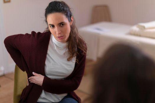 A female patient talks to her therapist in the office, explaining her pain, so that she can offer her a treatment for her health