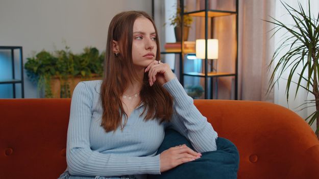Portrait of sad young woman sitting at home looks pensive thinks over life concerns or unrequited love, suffers from unfair situation. Problem, break up, depressed girl feeling bad annoyed, burnout