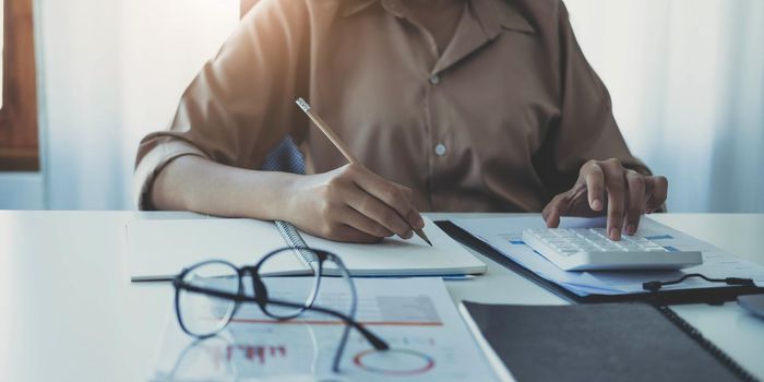 Business woman using calculator and writing make note with calculate. Woman working at office with laptop and documents on his desk.