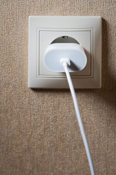 Electric socket on a pink wall. The black wire plug is connected. Renovated backdrop of studio apartment. Blank copy space single white plastic socket.