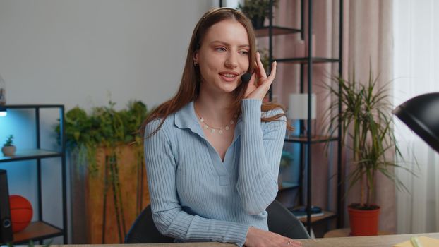 Young business woman sitting at desk at home office wearing headset, freelance worker, call center or support service operator helpline, having talk with client or colleague, communication support