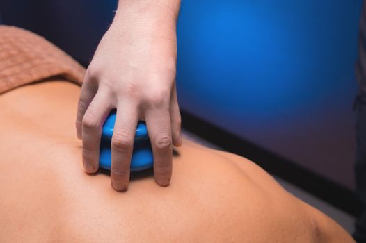 The concept of a healthy body. Hand putting a blue rubber jar for massage on a man's back. Close-up.