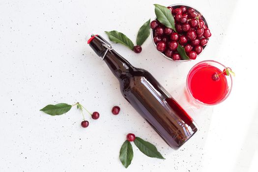 Cold cherry juice in a glass and bottle with ripe berries. Top view, copy space for text. The concept of summer refreshing drink morse or kompot.