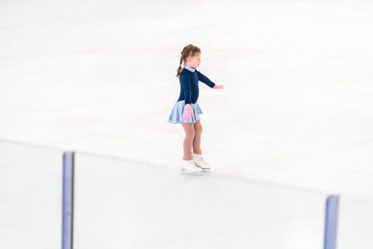 Little girl practicing figure skating on an indoor ice skating rink.