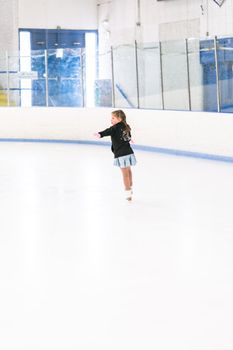 Little girl practicing figure skating on an indoor ice skating rink.