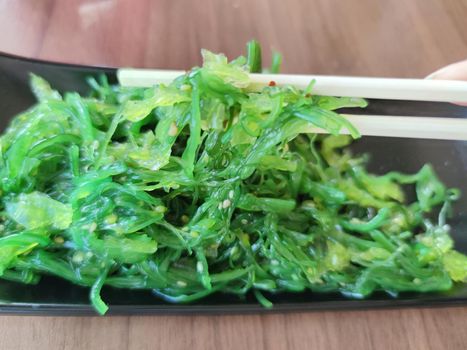 wakame seaweed salad with sesame seeds and japanese wooden sticks close-up