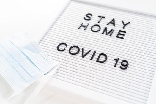 STAY HOME and COVID-19 sign on message board with a blue medical mask.