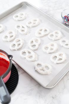 Dipping pretzels twists into melted chocolate to make red, white, and blue chocolate-covered pretzel twists.