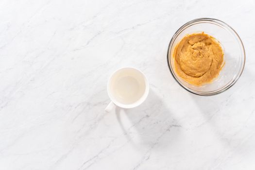 Flat lay. Pouring cake batter into the mug to prepare pumpkin mug cake.