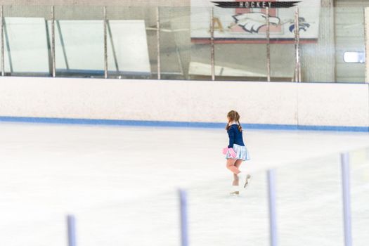 Little girl practicing figure skating on an indoor ice skating rink.