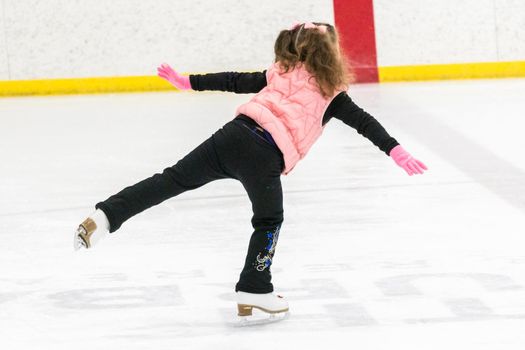 Little girl practicing figure skating moves on the indoor ice rink.