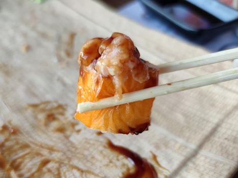 wooden japanese chopsticks hold sushi in teriyaki sauce close-up