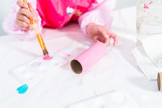 Little girl making a unicorn out of the toilet paper roll and craft paper.