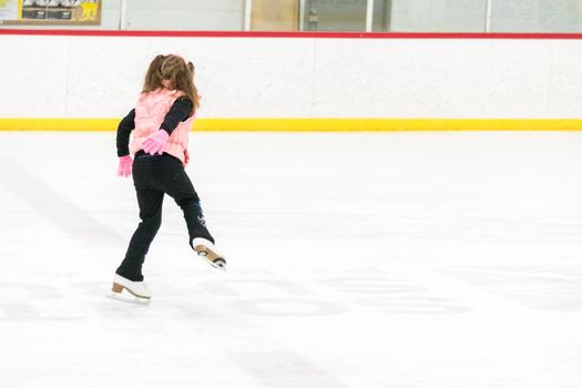 Little girl practicing figure skating moves on the indoor ice rink.