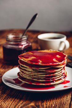 Stack of american pancakes with red berry jam on plate over rustic surface