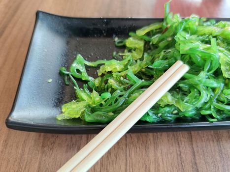 wakame seaweed salad with sesame seeds and japanese wooden sticks close-up