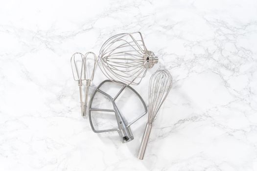 Flat lay. Variety of blending whisks on a marble countertop.