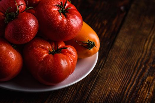 Fresh red and yellow tomatoes on white plate over wooden surface