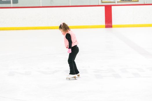 Little girl practicing figure skating moves on the indoor ice rink.