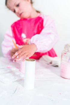 Little girl making a unicorn out of the toilet paper roll and craft paper.