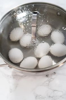 Boiling white eggs in a cooking pot to prepare hard-boiled eggs.