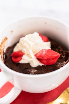 Chocolate mug cakes garnished with whipped cream and chocolate hearts and lips.