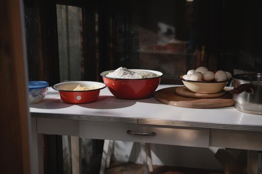 Assortment of fresh pizza ingredients in enamel vintage bowls on a white table in a rustic country house kitchen. Food still life. Raising yeast whole grain dough, fresh vegetables and grated cheese