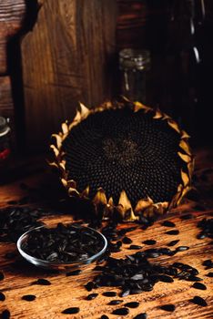 Roasted seeds on the glass saucer and dried sunflower over old wooden surface