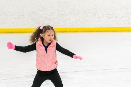 Little girl practicing figure skating moves on the indoor ice rink.