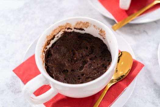 Freshly baked chocolate mug cakes in white cups.