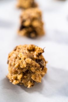 Scooping cookie dough with dough scoop into a baking sheet lined with parchment paper to bake soft oatmeal raisin walnut cookies.