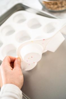 Scooping dough with dough scoop into cupcake pan lined with tulip paper muffin liners to bake banana oatmeal muffins.