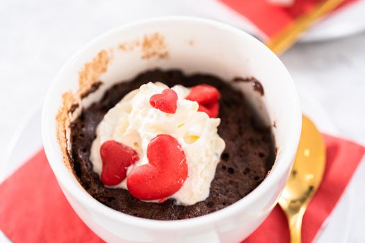 Chocolate mug cakes garnished with whipped cream and chocolate hearts and lips.