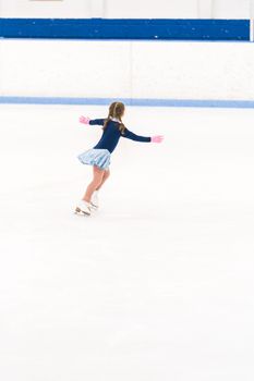 Little girl practicing figure skating on an indoor ice skating rink.