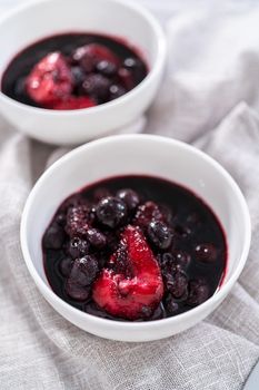 Homemade mix berry compote in small white bowls on a wooden table.