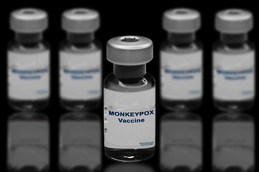 Monkeypox vaccine close-up on a black mirror background. In the background are blurred vaccine vials.